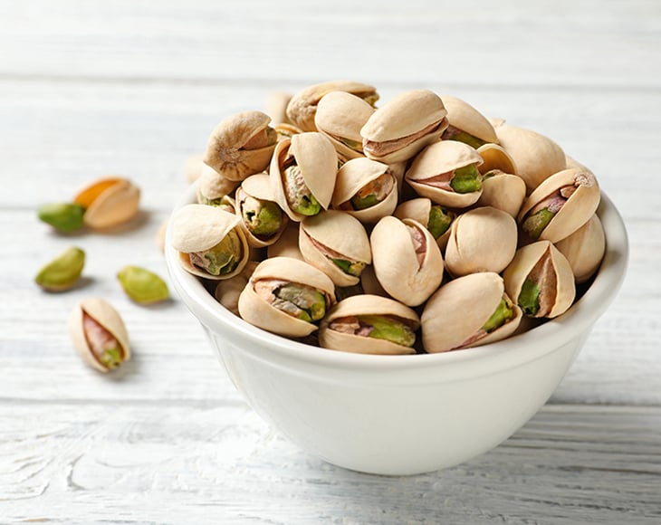Roasted and salted pistachio nuts in bowl on wooden table, closeup